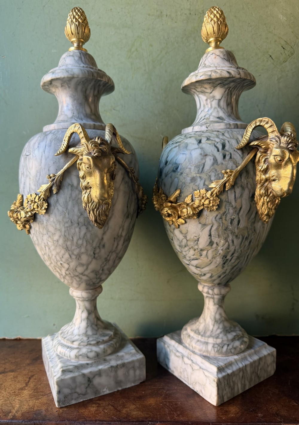 A pair of late 19th-century French Louis XVI style Campan vert marble urns adorned with gilt bronze ram head handles, floral swags, and pinecone finials. View IX