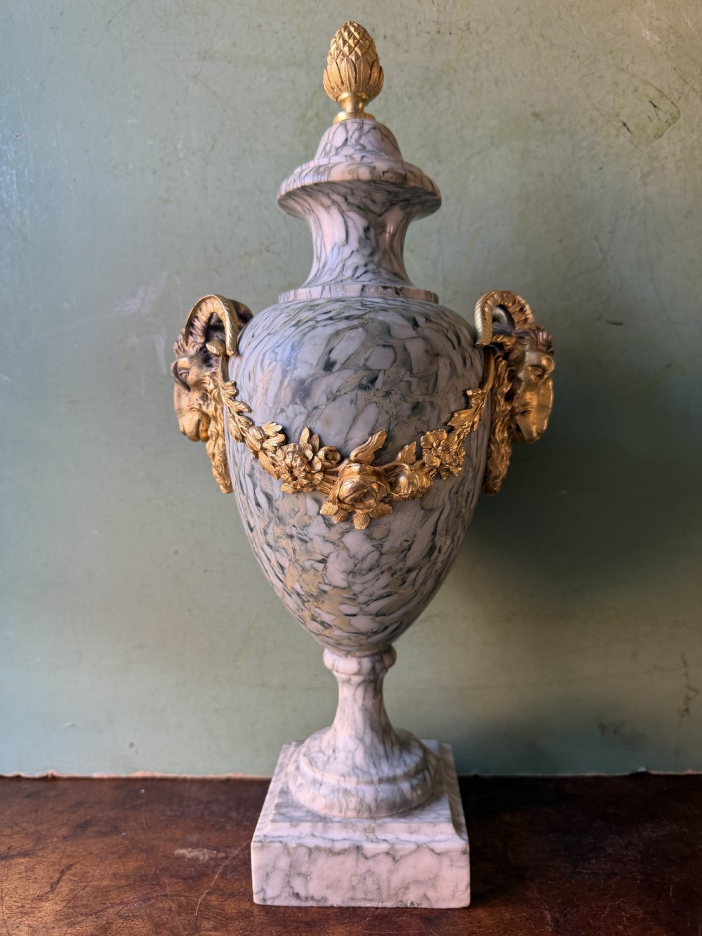 A pair of late 19th-century French Louis XVI style Campan vert marble urns adorned with gilt bronze ram head handles, floral swags, and pinecone finials. View X