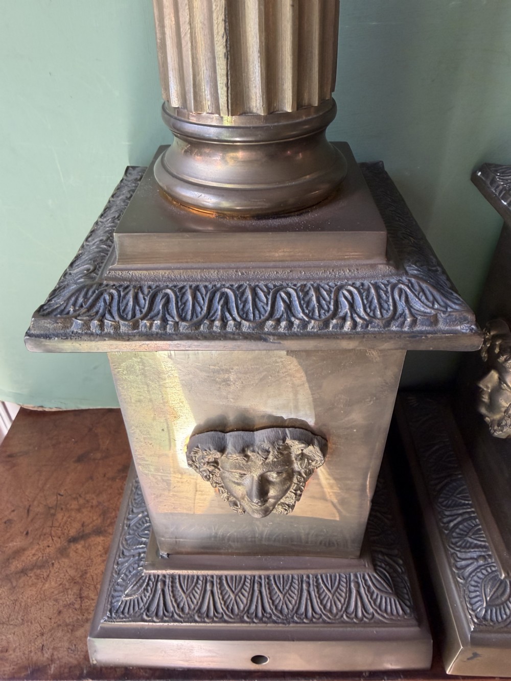 A pair of early twentieth-century brass table lamps featuring fluted classical columns, Corinthian capitals, and square pedestal bases decorated with cast face masks. View VIII