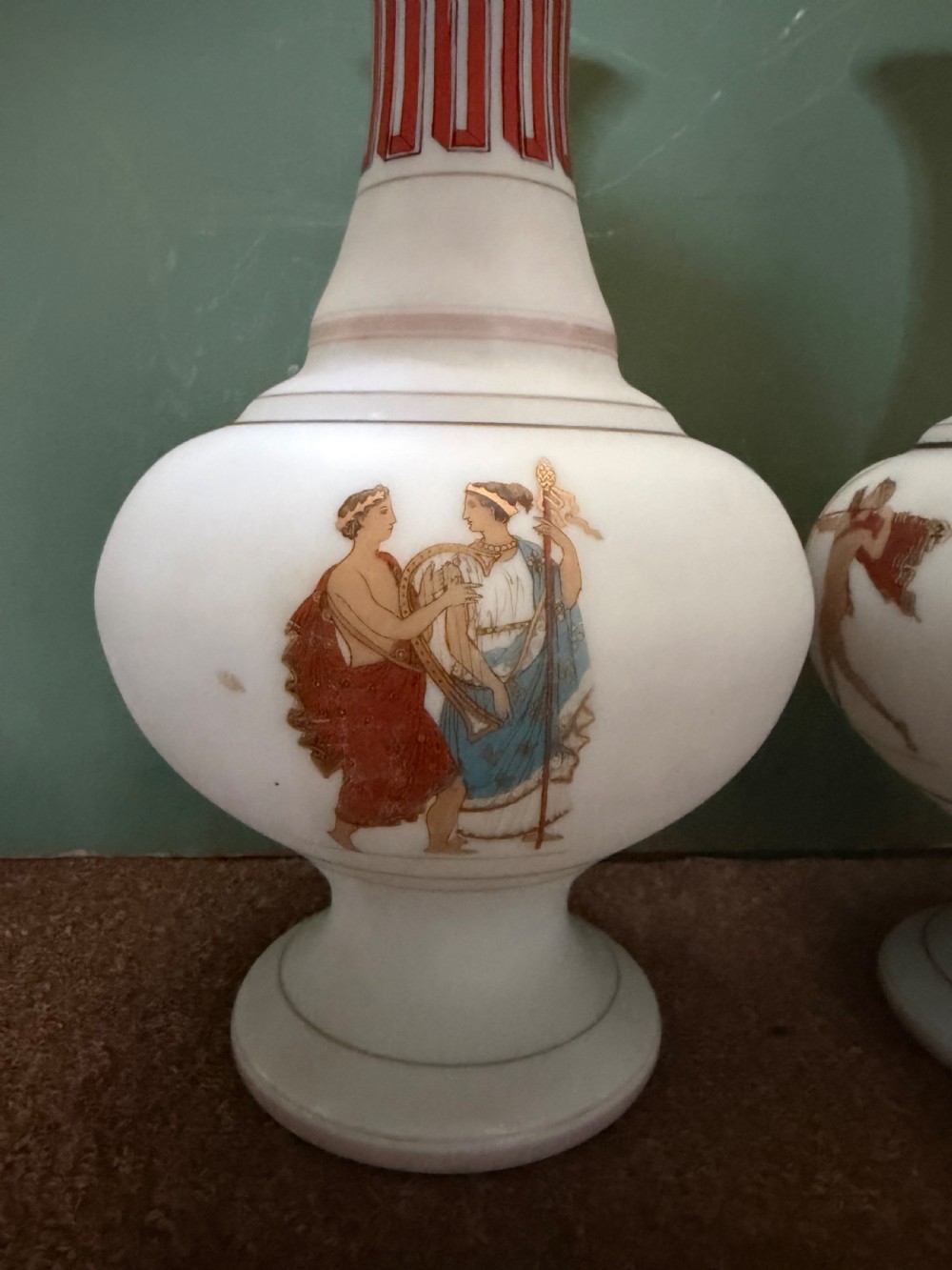 A pair of white opaline glass vases featuring flared necks decorated with orange Greek key patterns and baluster bodies painted with classical Grecian warrior figures. View V
