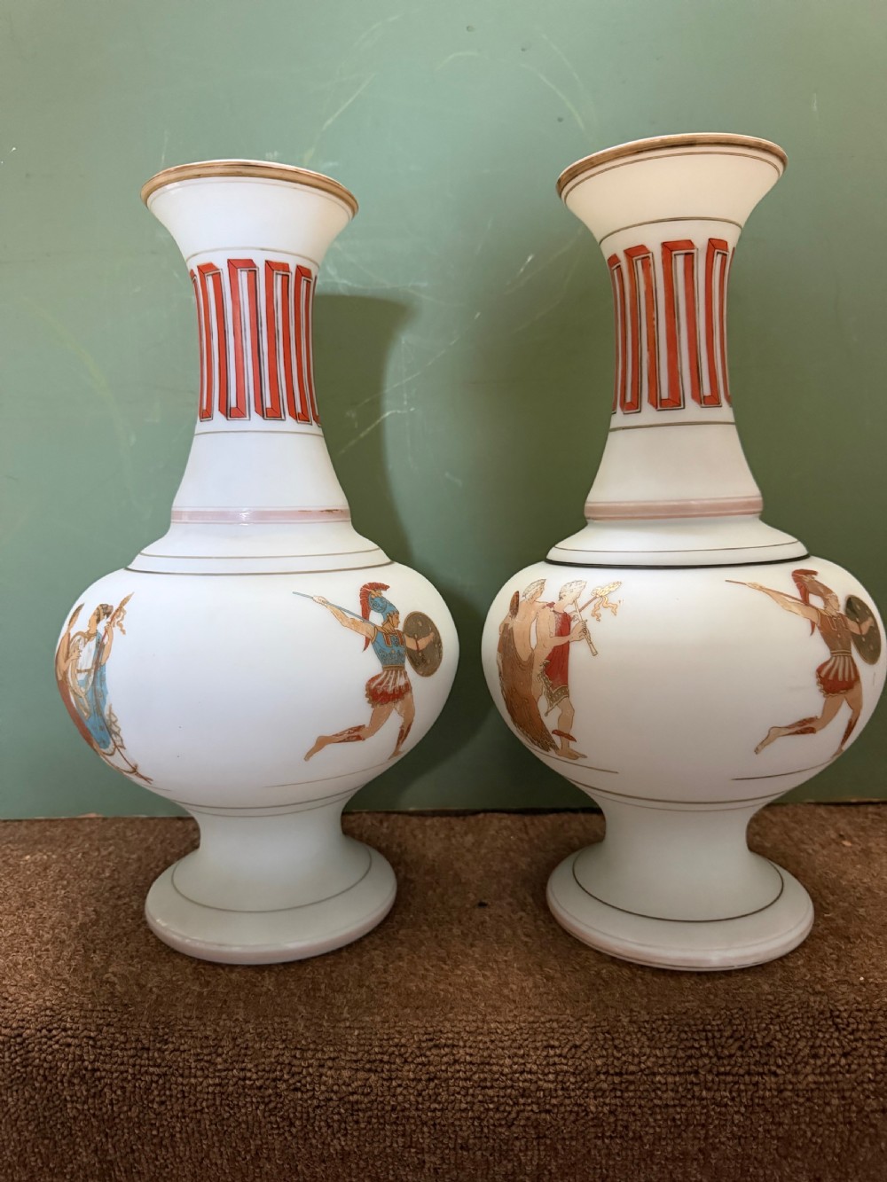 A pair of white opaline glass vases featuring flared necks decorated with orange Greek key patterns and baluster bodies painted with classical Grecian warrior figures. View VIII