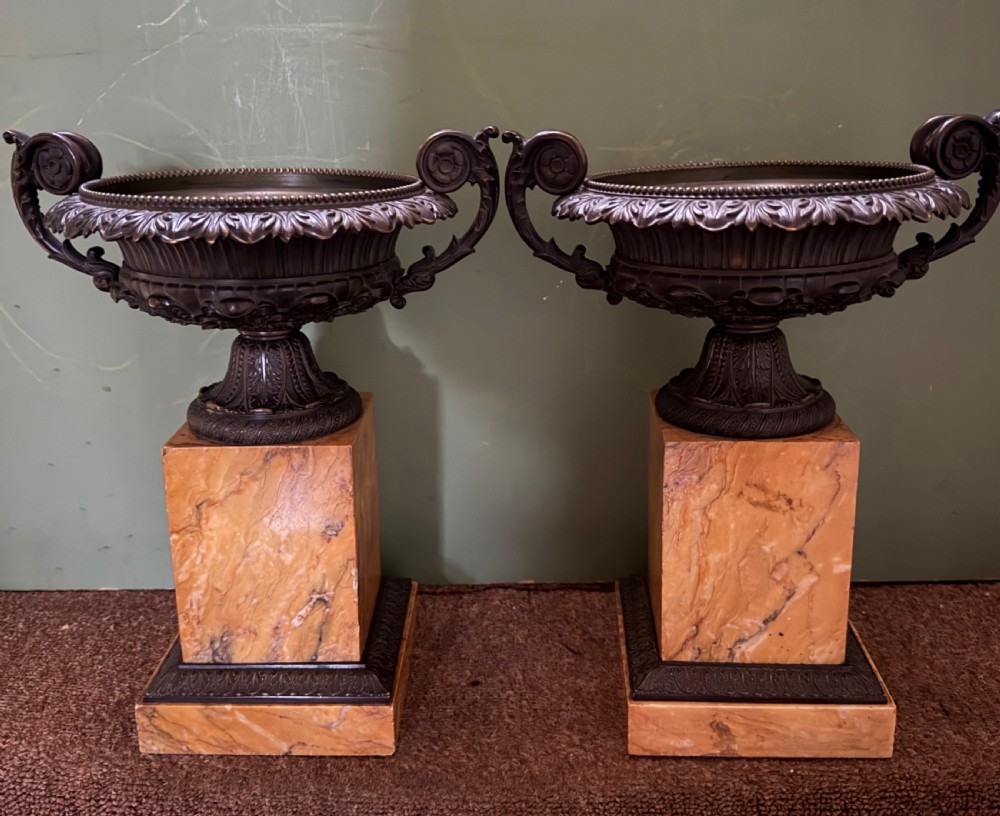 A pair of early 19th-century French Charles X dark bronze tazze with scrolling handles set upon yellow Siena marble plinth bases.
