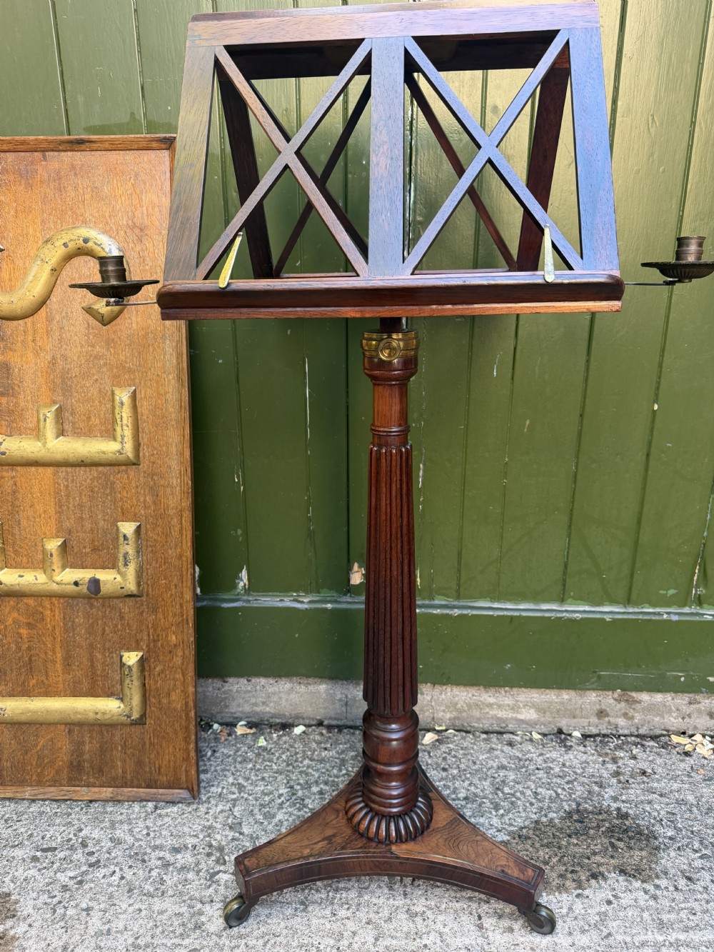 An early 19th-century Regency rosewood duet music stand featuring an adjustable double-sided frame with cross-latticed supports, twin brass candle sconces, a fluted column, and a tripartite base on castors. View II