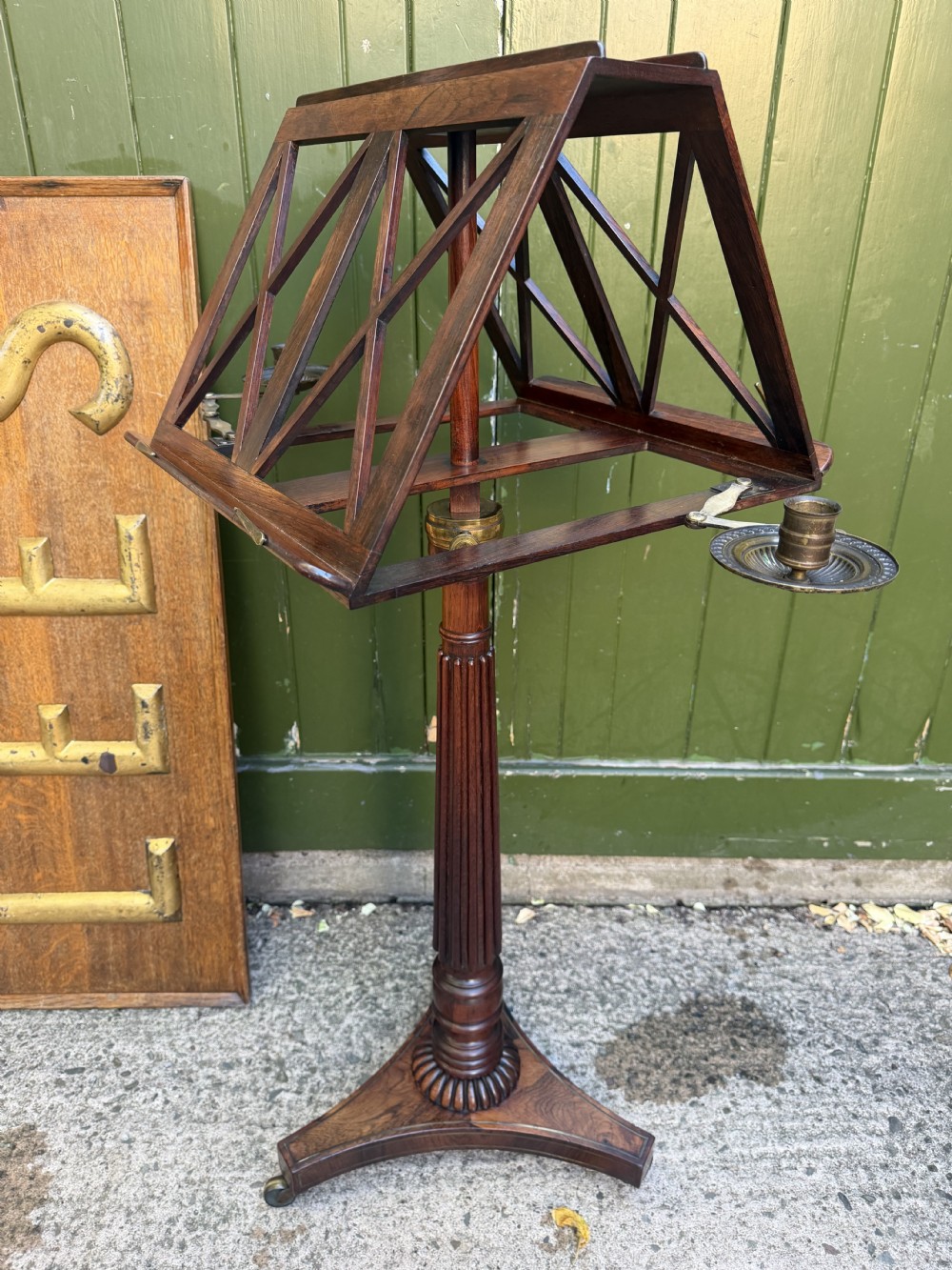 An early 19th-century Regency rosewood duet music stand featuring an adjustable double-sided frame with cross-latticed supports, twin brass candle sconces, a fluted column, and a tripartite base on castors. View VI