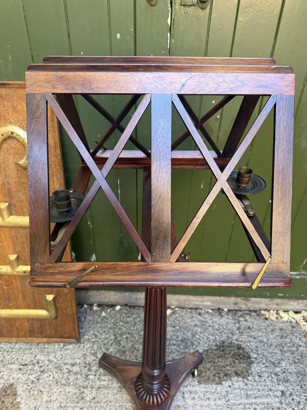 An early 19th-century Regency rosewood duet music stand featuring an adjustable double-sided frame with cross-latticed supports, twin brass candle sconces, a fluted column, and a tripartite base on castors. View XII