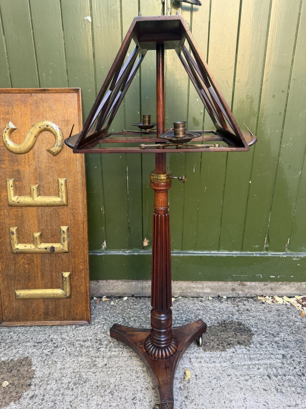 An early 19th-century Regency rosewood duet music stand featuring an adjustable double-sided frame with cross-latticed supports, twin brass candle sconces, a fluted column, and a tripartite base on castors. View XVIII