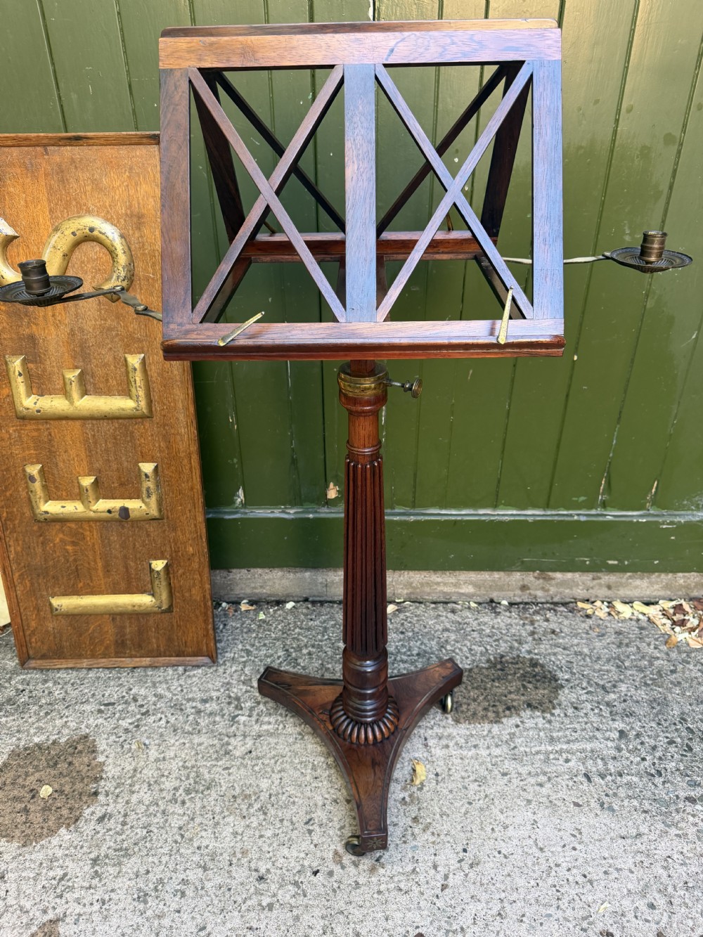 An early 19th-century Regency rosewood duet music stand featuring an adjustable double-sided frame with cross-latticed supports, twin brass candle sconces, a fluted column, and a tripartite base on castors. View XXI