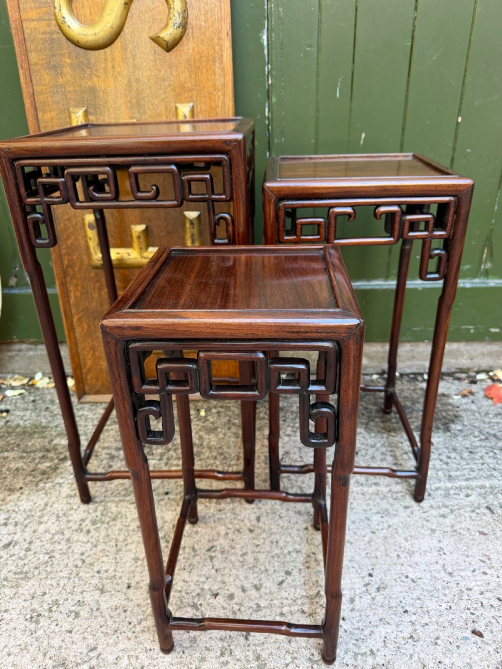 A set of three graduated dark hardwood Chinese nesting tables featuring openwork carved fretwork aprons and straight legs with perimeter stretchers. View III