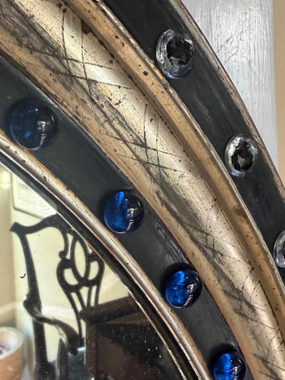 A nineteenth-century Irish oval wall mirror featuring an ebonised frame inset with clear facetted glass jewels, an inner silver-gilt band, and cobalt blue glass cabochons. View V