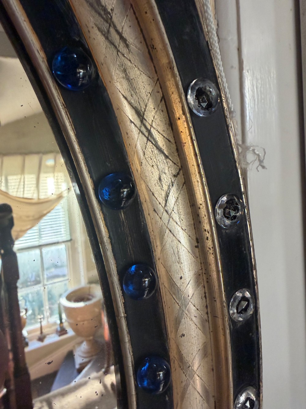 A nineteenth-century Irish oval wall mirror featuring an ebonised frame inset with clear facetted glass jewels, an inner silver-gilt band, and cobalt blue glass cabochons. View X