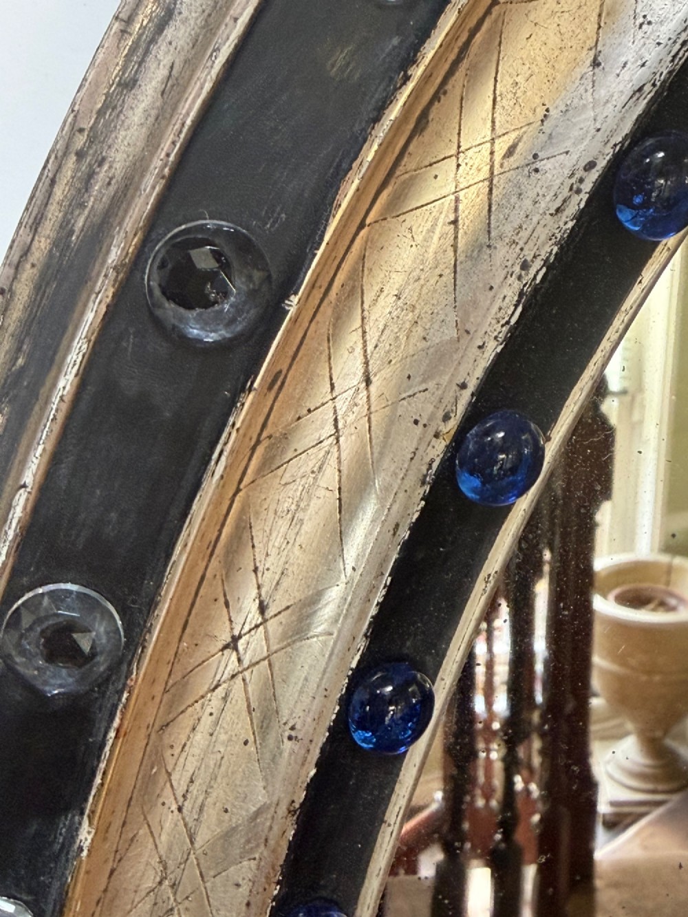 A nineteenth-century Irish oval wall mirror featuring an ebonised frame inset with clear facetted glass jewels, an inner silver-gilt band, and cobalt blue glass cabochons. View XII