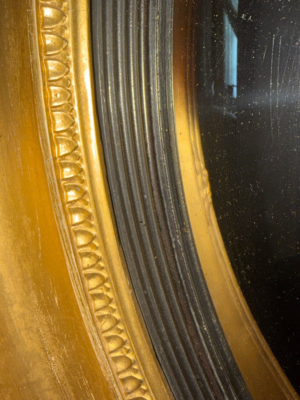 A circular early 19th-century Regency convex mirror featuring a gilded carved frame with an ebonised inner reeded slip. View IV