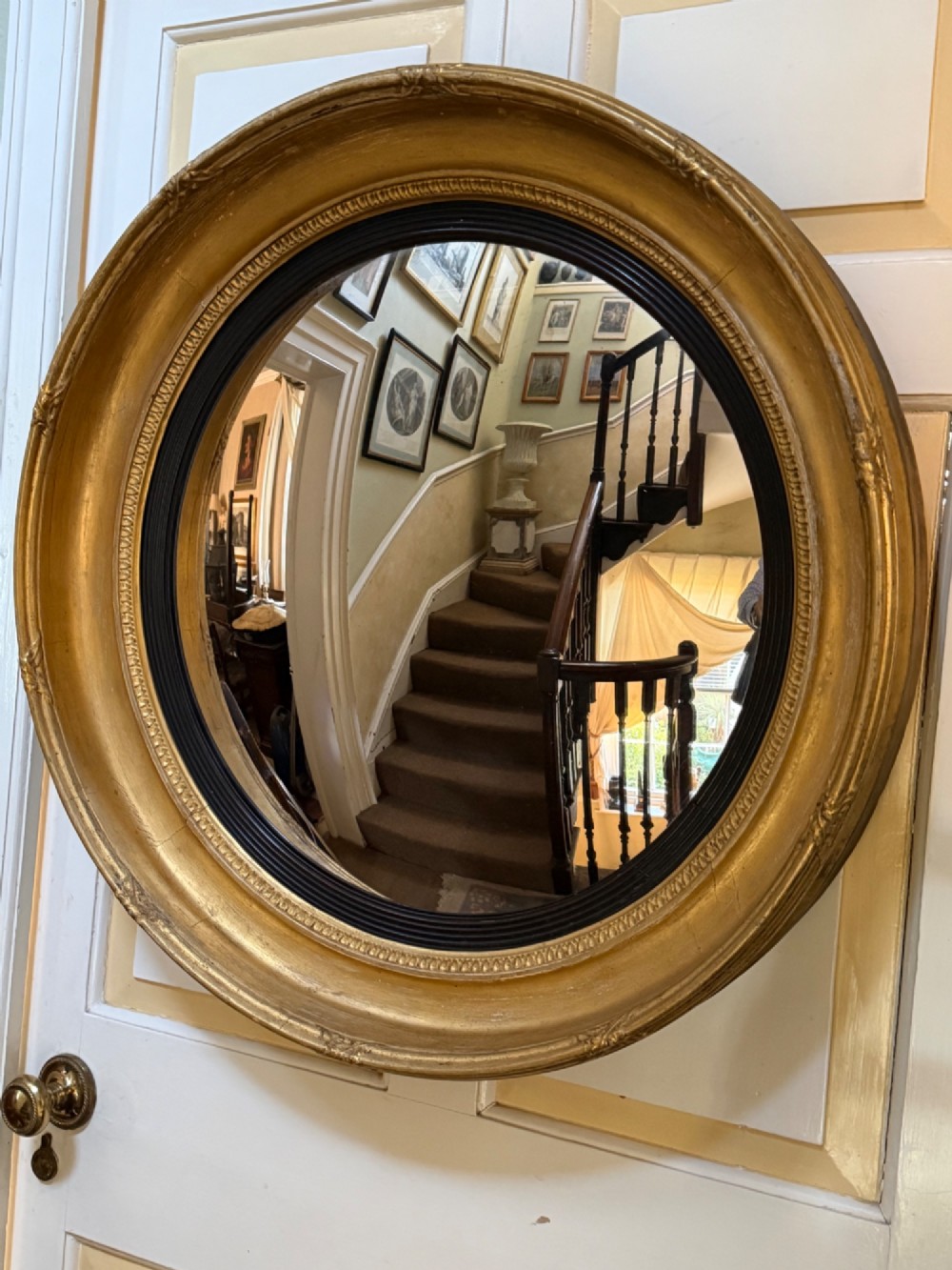 A circular early 19th-century Regency convex mirror featuring a gilded carved frame with an ebonised inner reeded slip. View IX