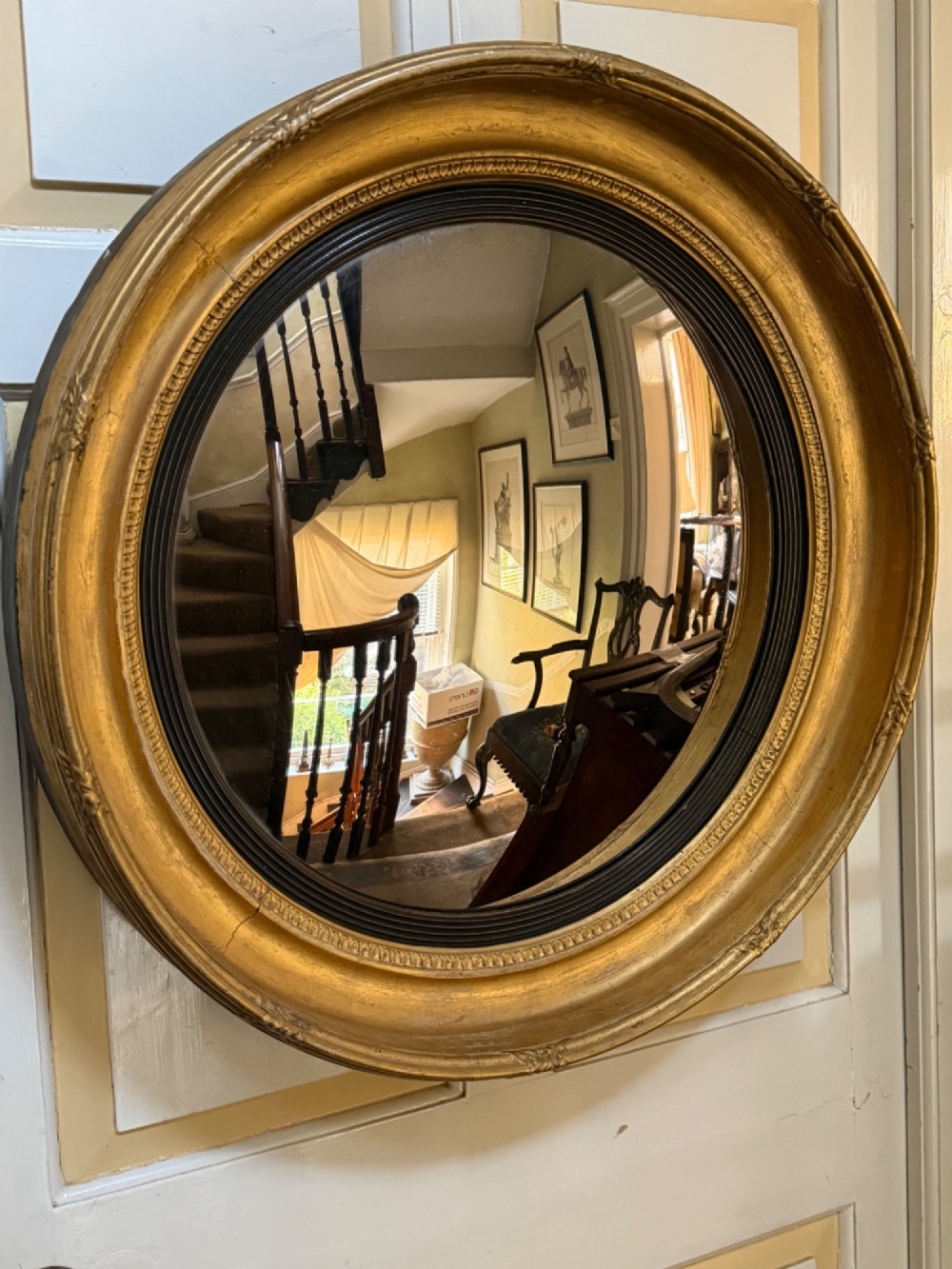 A circular early 19th-century Regency convex mirror featuring a gilded carved frame with an ebonised inner reeded slip. View X