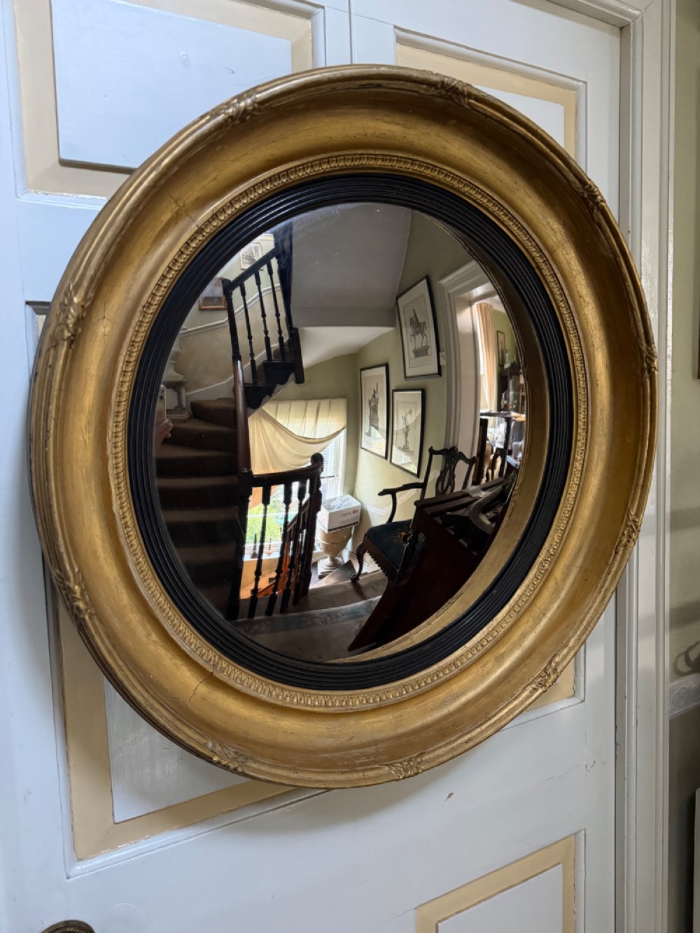 A circular early 19th-century Regency convex mirror featuring a gilded carved frame with an ebonised inner reeded slip. View XII