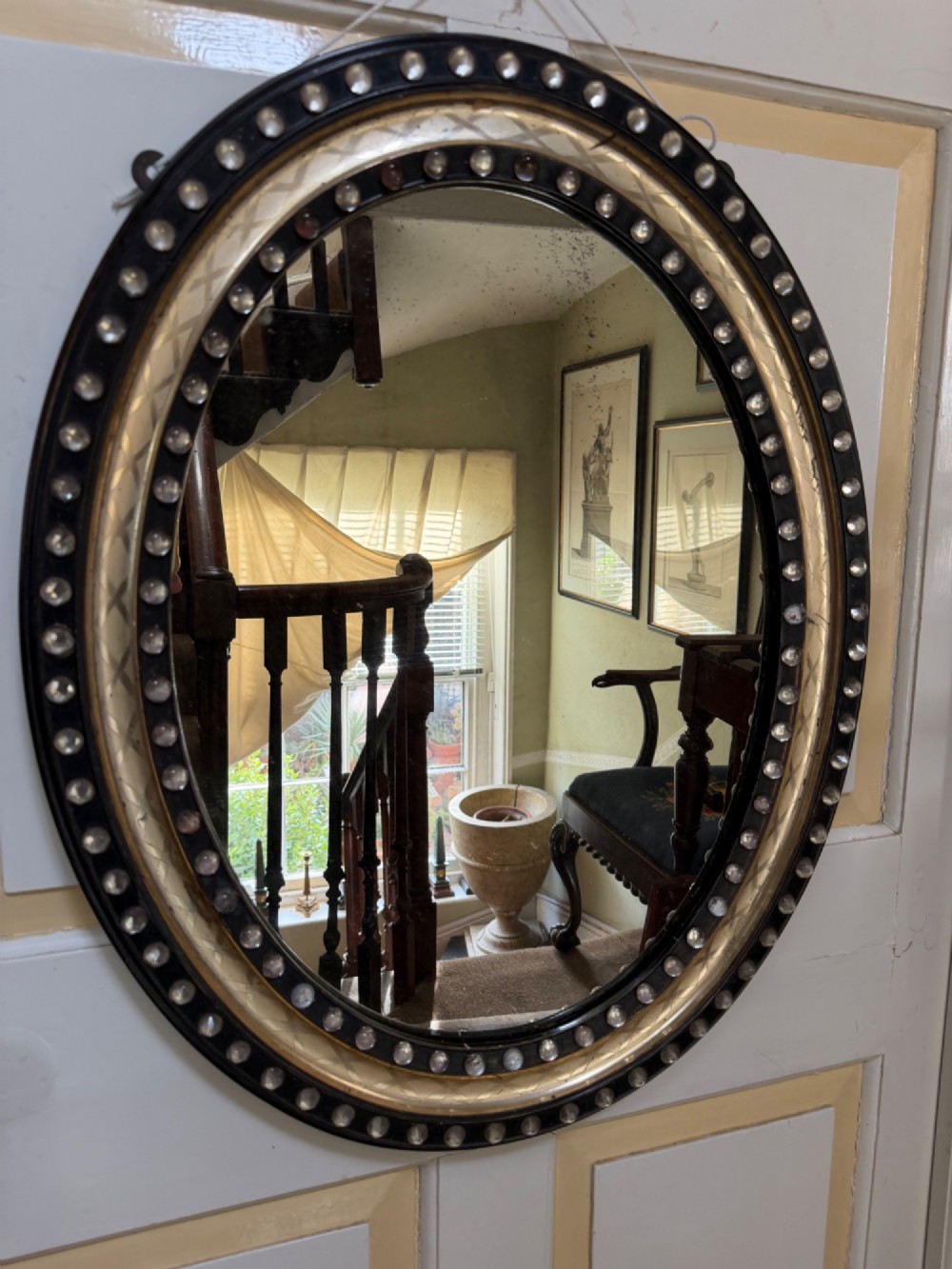 An early nineteenth-century Irish oval wall mirror featuring an ebonised and silver-gilt frame embellished with an outer border of faceted glass cabochons. View II
