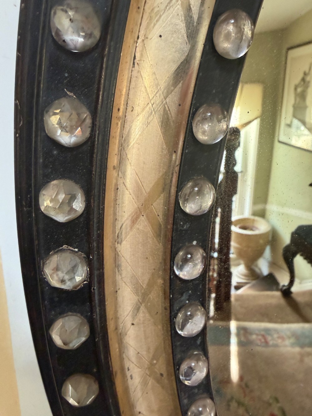An early nineteenth-century Irish oval wall mirror featuring an ebonised and silver-gilt frame embellished with an outer border of faceted glass cabochons. View V