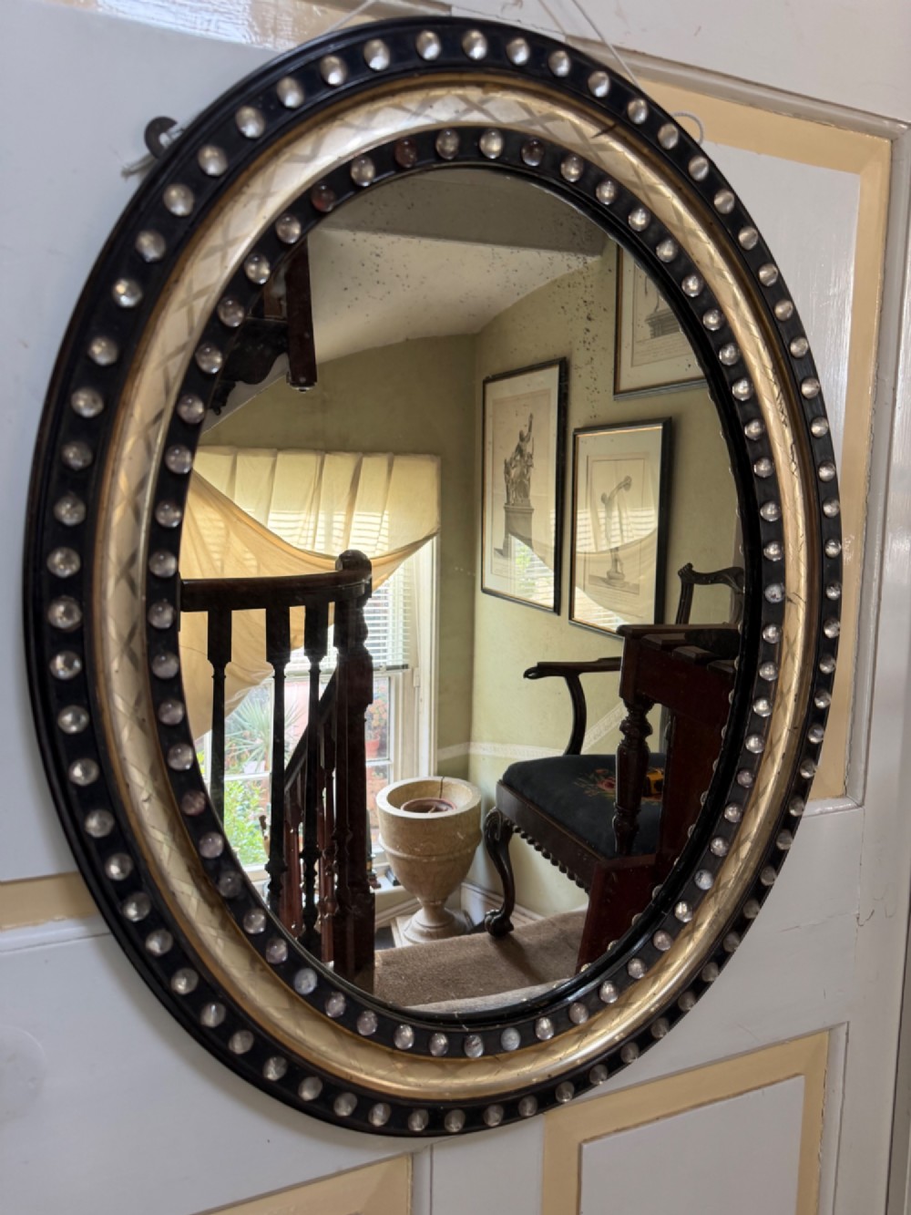 An early nineteenth-century Irish oval wall mirror featuring an ebonised and silver-gilt frame embellished with an outer border of faceted glass cabochons. View VI