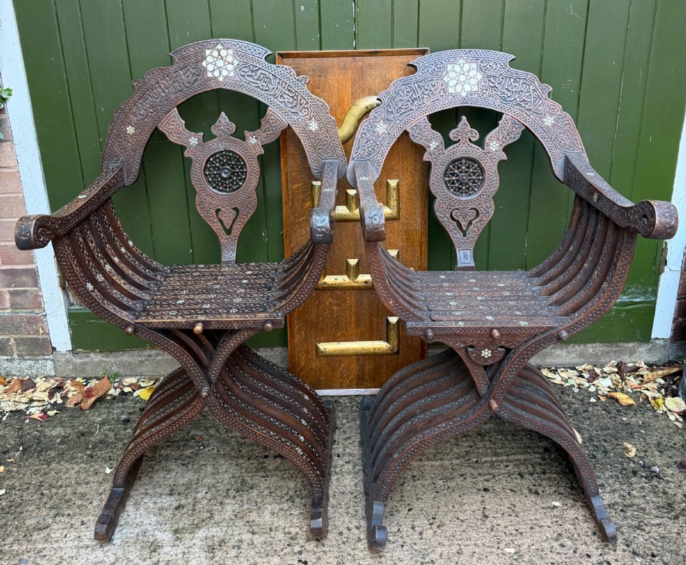A pair of late nineteenth-century Syrian armchairs crafted from dark carved wood with mother-of-pearl inlay, Arabic script panels, and curule x-frames. View II