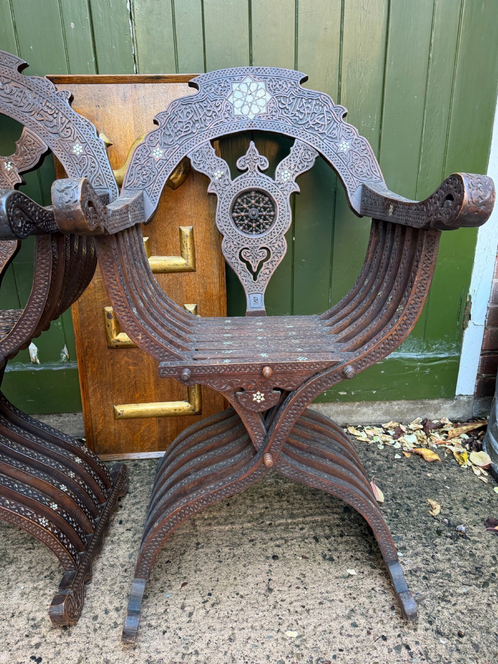 A pair of late nineteenth-century Syrian armchairs crafted from dark carved wood with mother-of-pearl inlay, Arabic script panels, and curule x-frames. View VII