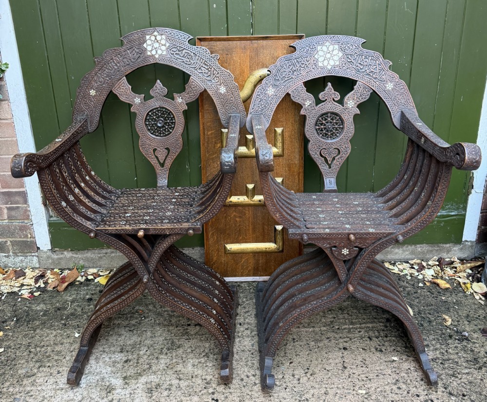 A pair of late nineteenth-century Syrian armchairs crafted from dark carved wood with mother-of-pearl inlay, Arabic script panels, and curule x-frames.