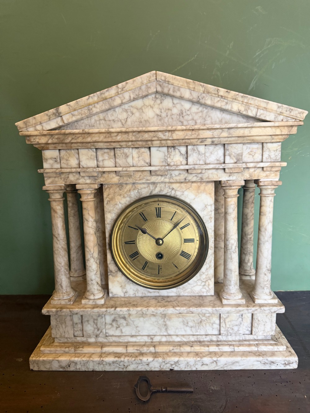 A late nineteenth-century carved cream alabaster mantel clock styled as a classical Greek temple with columns and a central brass dial.