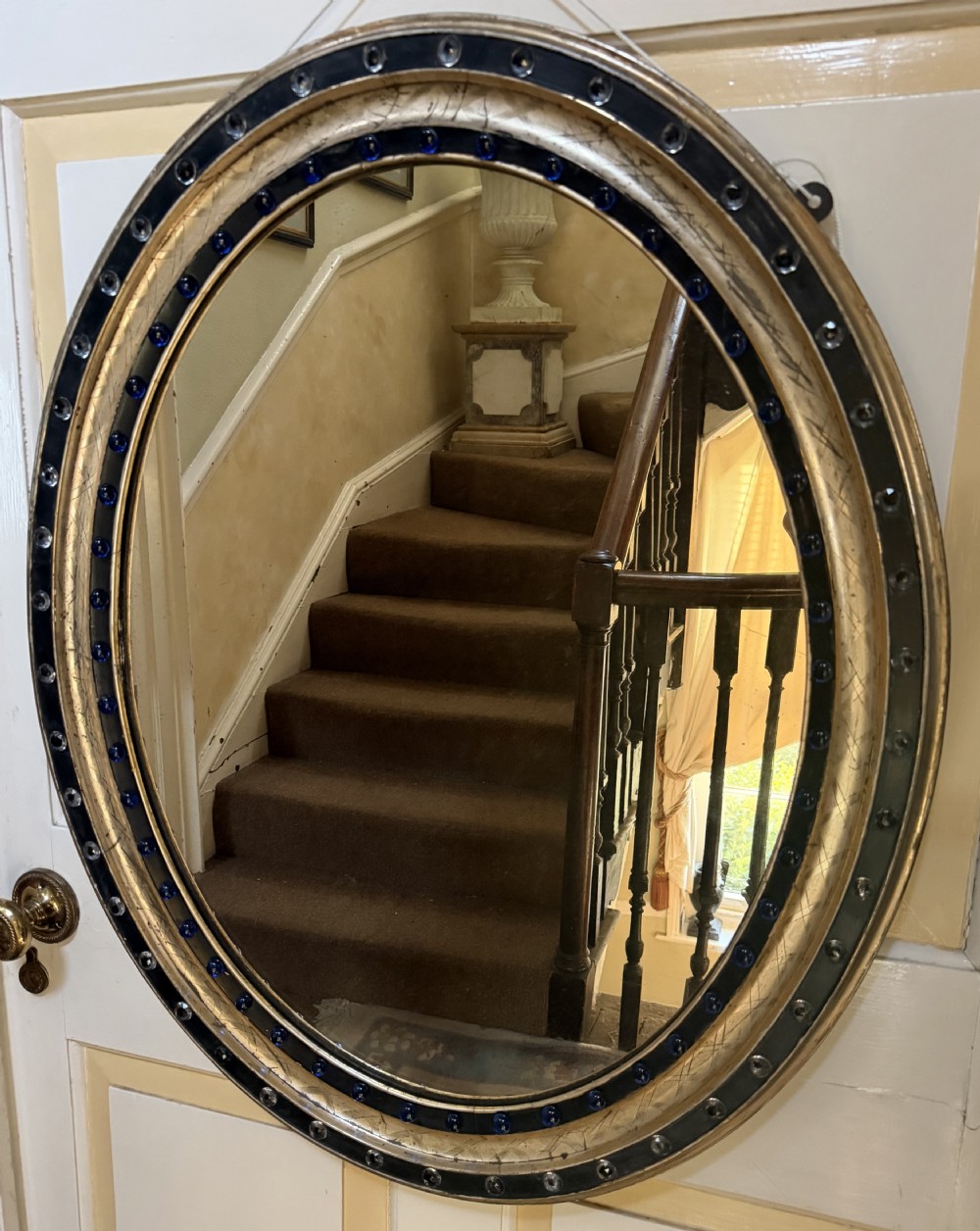 A nineteenth-century Irish oval wall mirror featuring an ebonised frame inset with clear facetted glass jewels, an inner silver-gilt band, and cobalt blue glass cabochons.