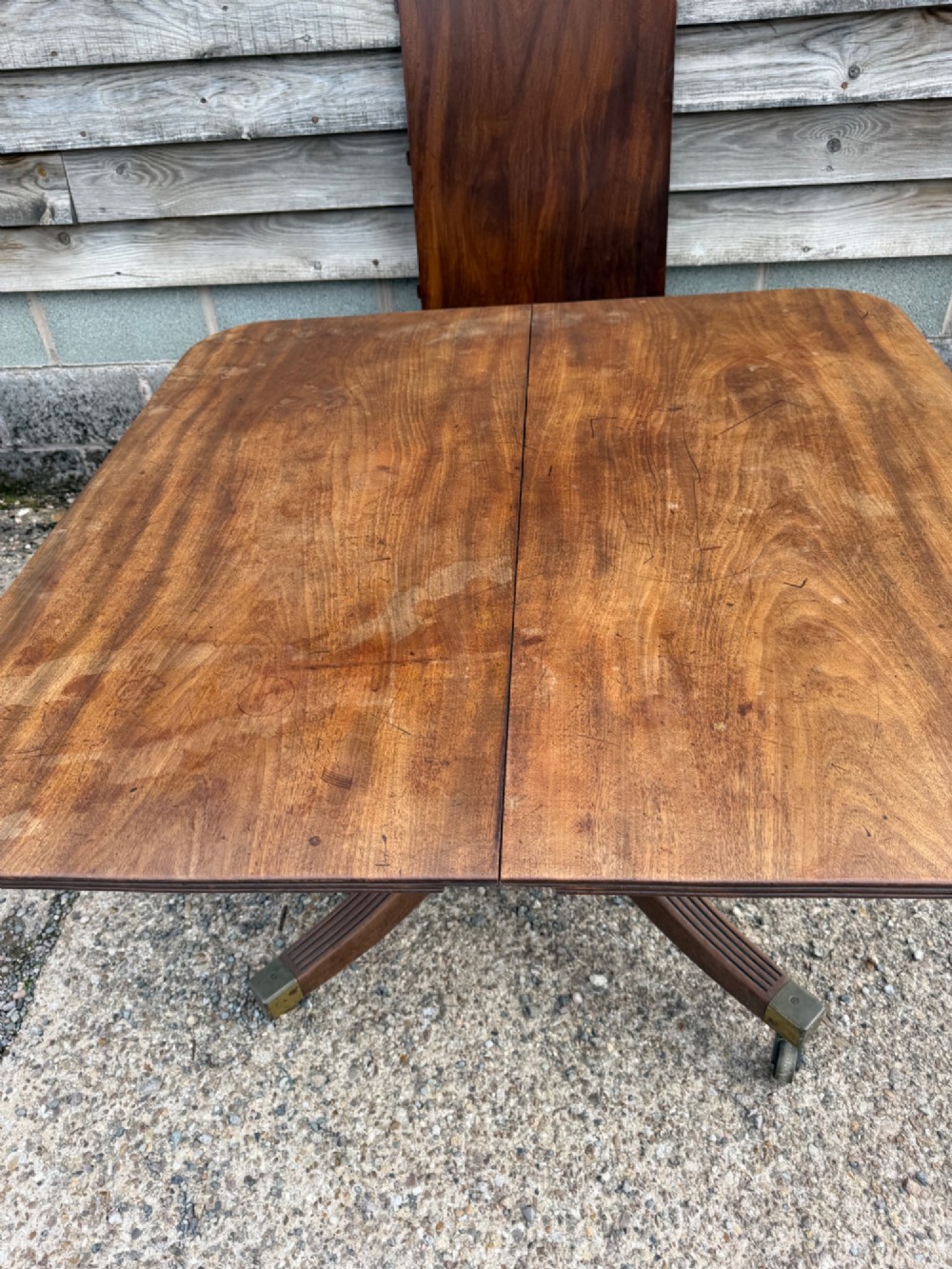 An early nineteenth-century mahogany extending dining table featuring a central reeded pedestal base with brass castors and an extra extension leaf standing behind. View II