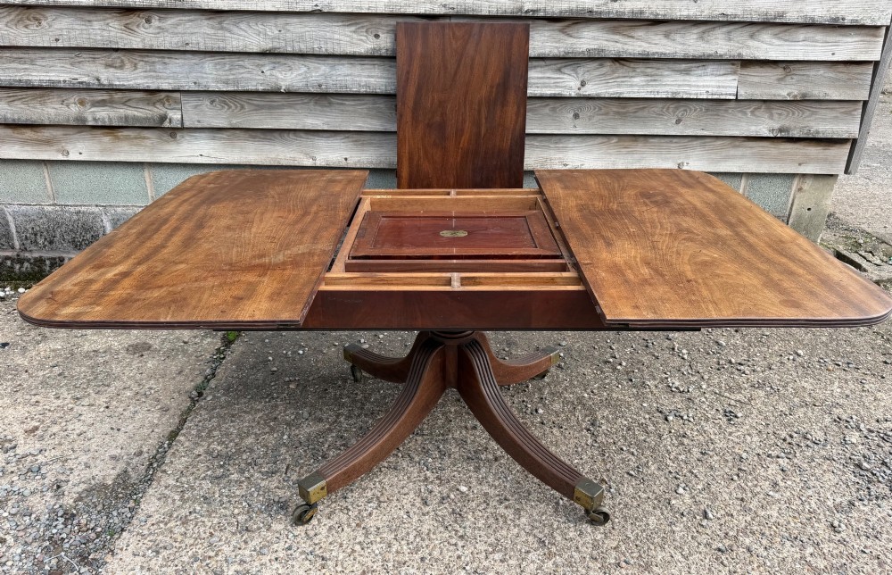 An early nineteenth-century mahogany extending dining table featuring a central reeded pedestal base with brass castors and an extra extension leaf standing behind. View III