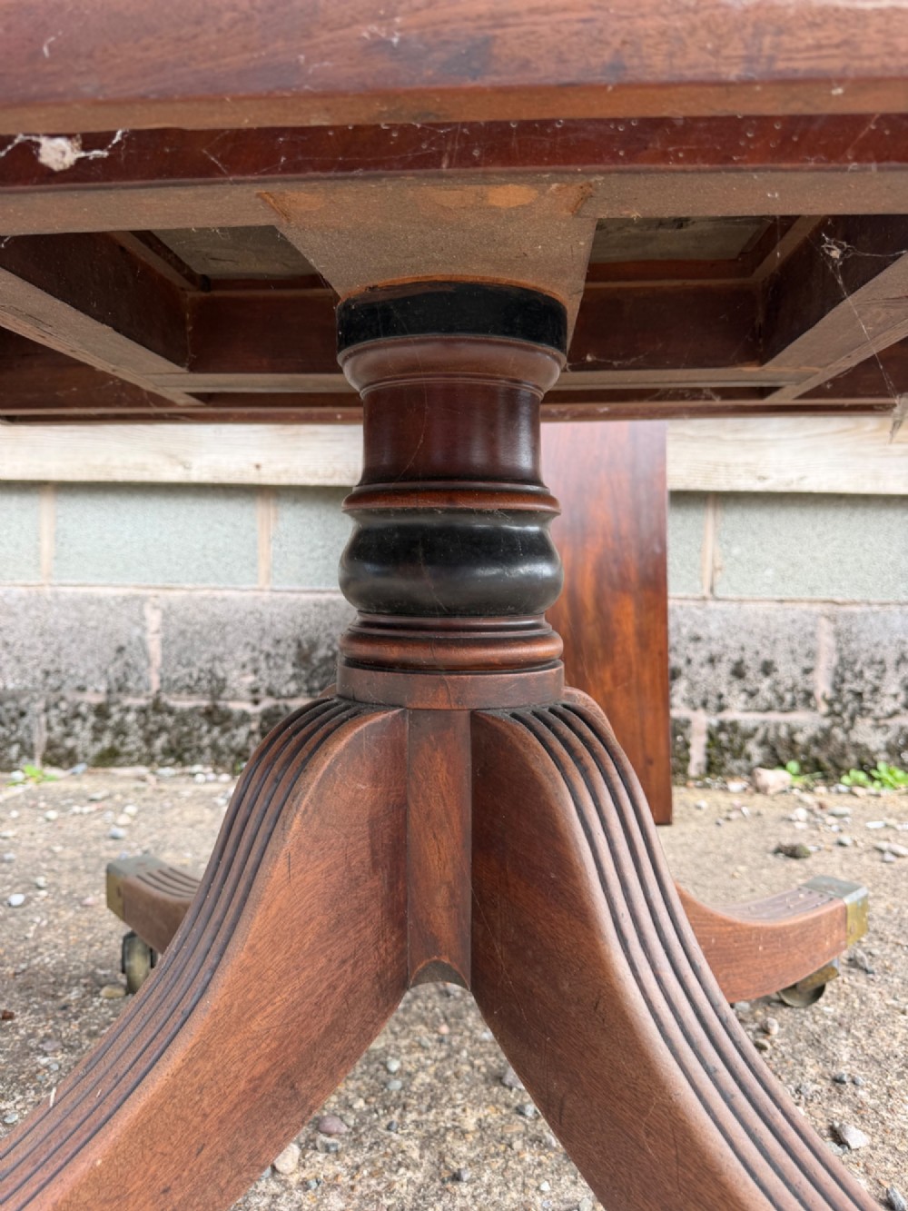 An early nineteenth-century mahogany extending dining table featuring a central reeded pedestal base with brass castors and an extra extension leaf standing behind. View IV