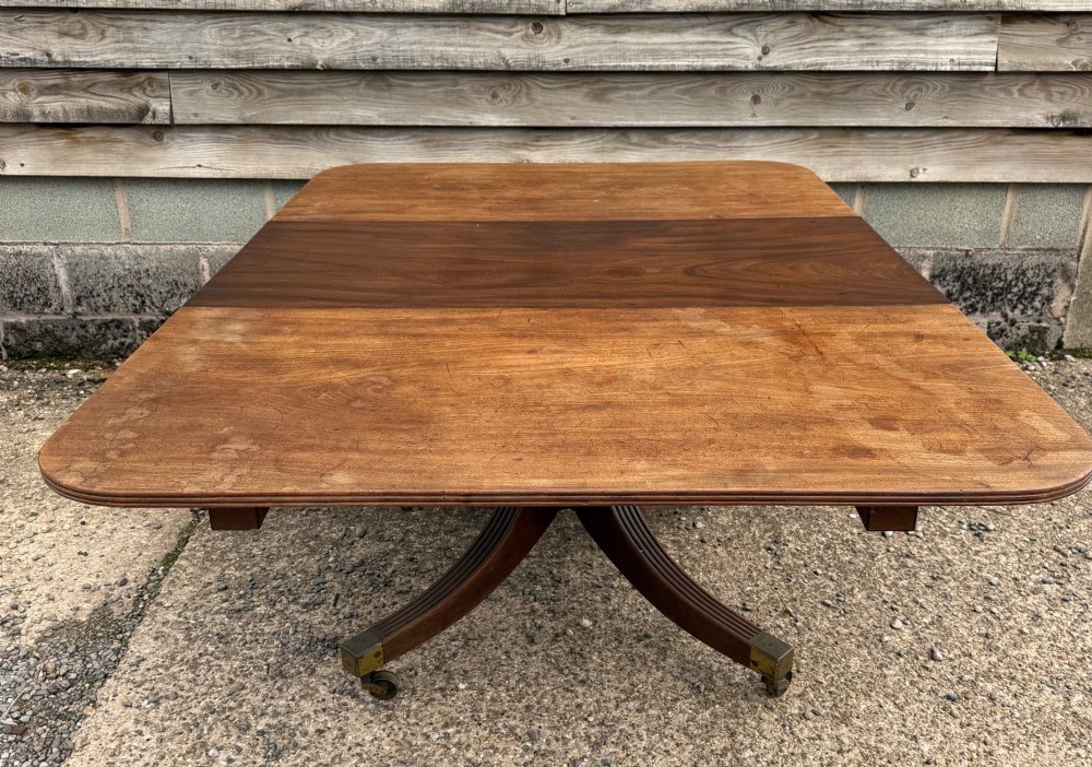An early nineteenth-century mahogany extending dining table featuring a central reeded pedestal base with brass castors and an extra extension leaf standing behind. View X