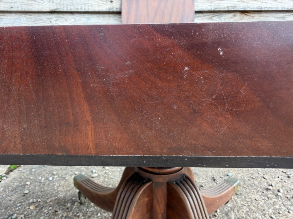 An early nineteenth-century mahogany extending dining table featuring a central reeded pedestal base with brass castors and an extra extension leaf standing behind. View XIII