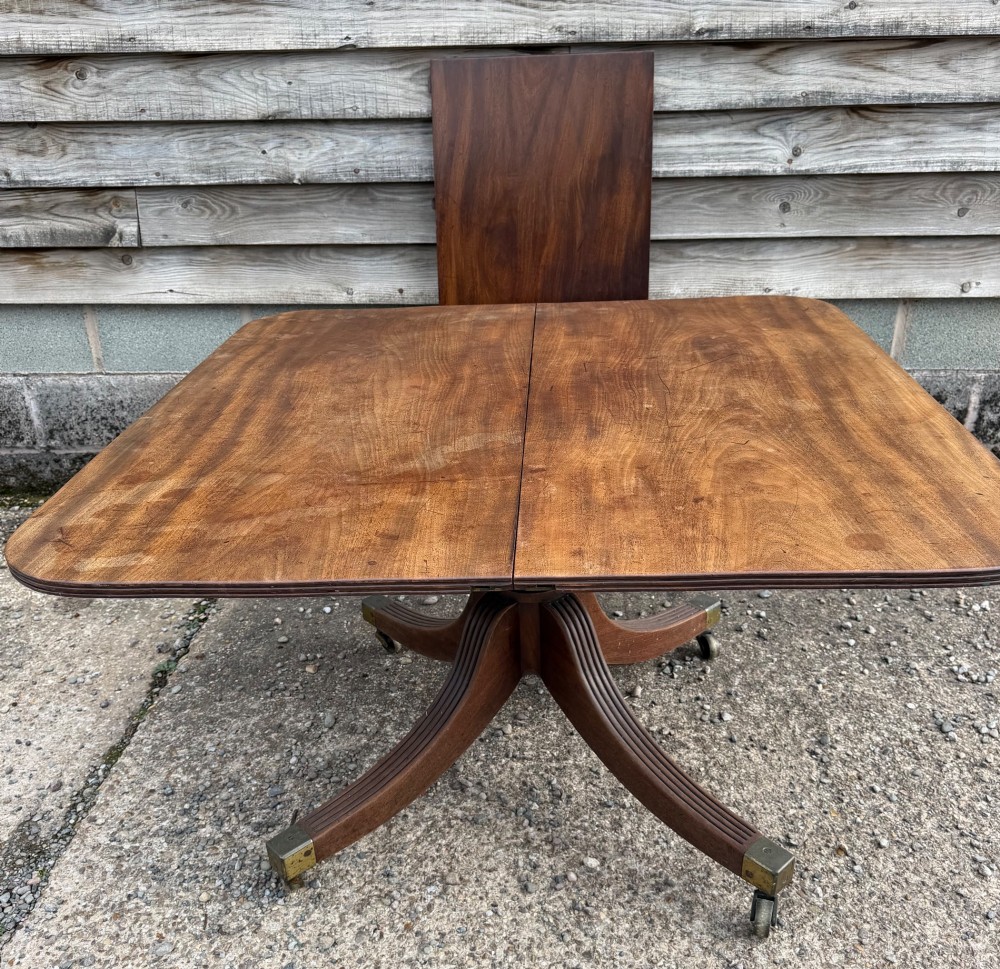An early nineteenth-century mahogany extending dining table featuring a central reeded pedestal base with brass castors and an extra extension leaf standing behind. View XIV