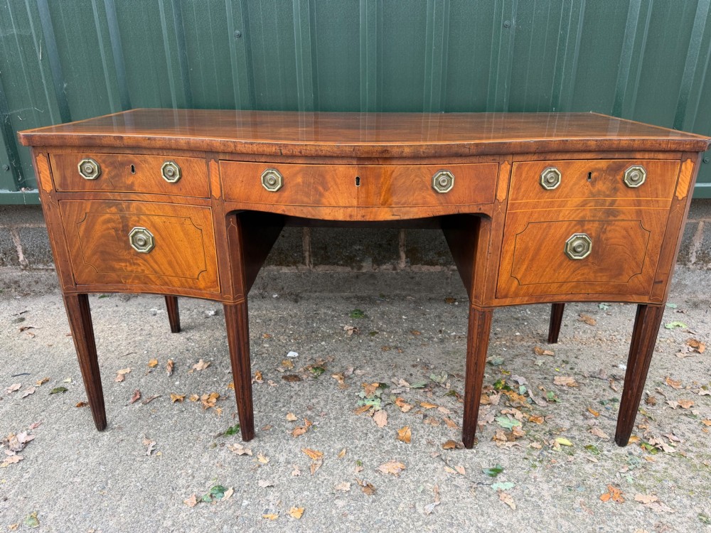 A late 18th-century George III mahogany sideboard featuring a serpentine front, stringing inlays, brass octagonal handles, and tapered square legs.