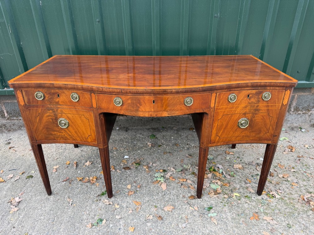 A late 18th-century George III mahogany sideboard featuring a serpentine front, stringing inlays, brass octagonal handles, and tapered square legs. View II