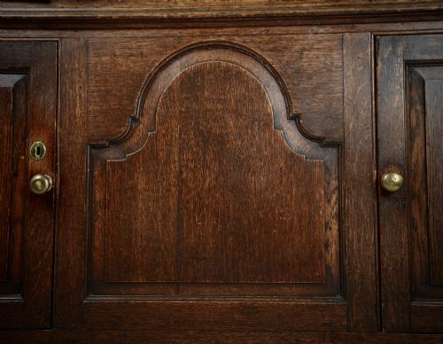 fig 1. An 18th-century dark oak dresser base featuring three drawers over two cupboard doors flanking a central arched fielded panel with brass hardware.