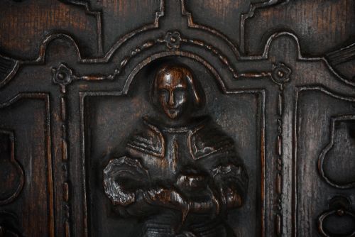 fig 1. A dark brown rectangular carved oak panel depicting a central relief figure in armour framed by intricate strapwork and decorative scrollwork.