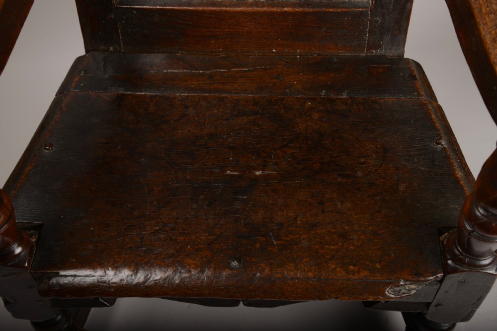 An early seventeenth-century dark oak wainscot armchair with a carved geometric panel back, turned arm supports, and a solid wooden seat. View XI