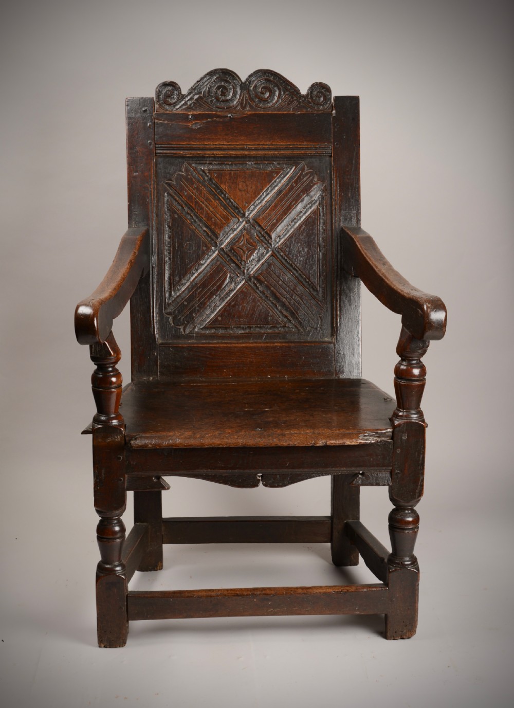 An early seventeenth-century dark oak wainscot armchair with a carved geometric panel back, turned arm supports, and a solid wooden seat. View II