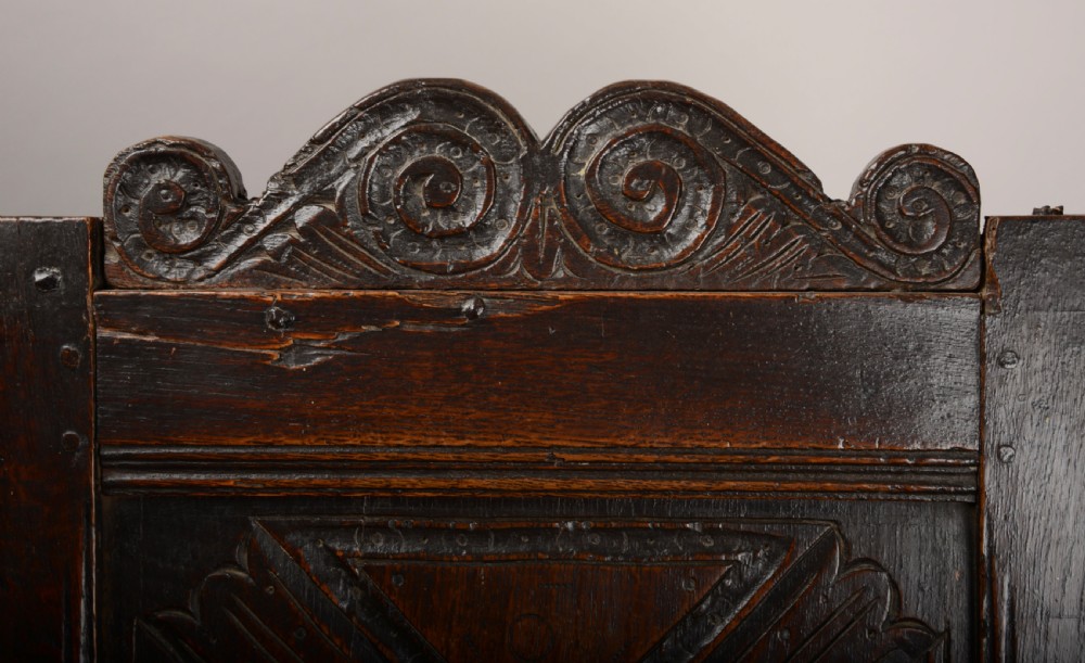 An early seventeenth-century dark oak wainscot armchair with a carved geometric panel back, turned arm supports, and a solid wooden seat. View III