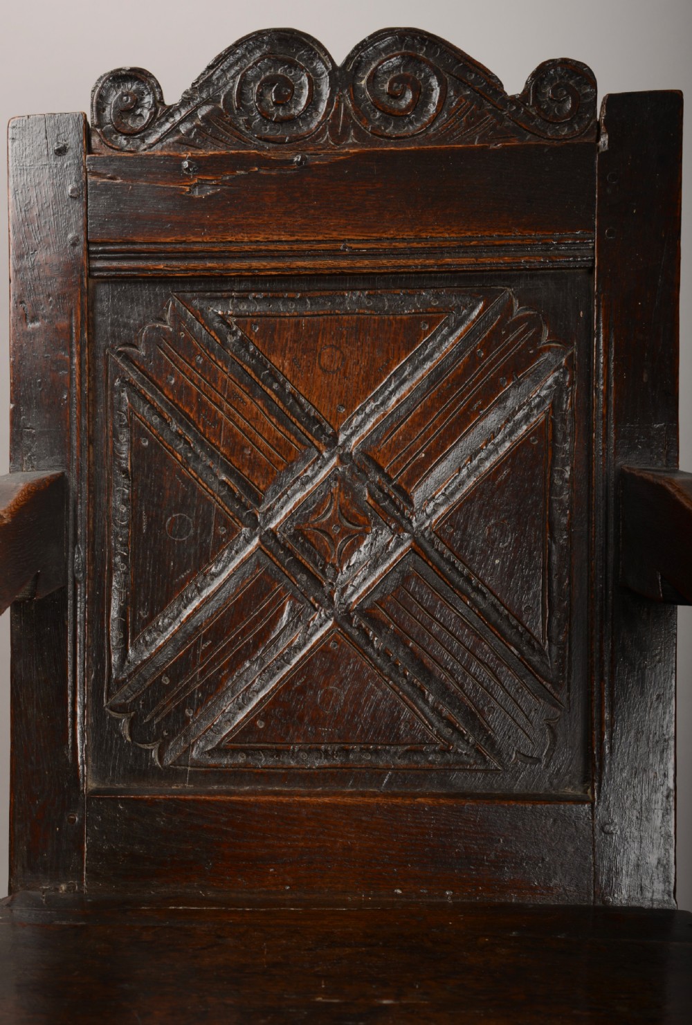 An early seventeenth-century dark oak wainscot armchair with a carved geometric panel back, turned arm supports, and a solid wooden seat. View IV