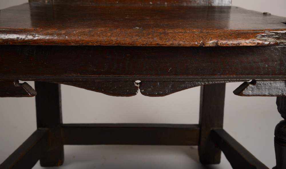 An early seventeenth-century dark oak wainscot armchair with a carved geometric panel back, turned arm supports, and a solid wooden seat. View V