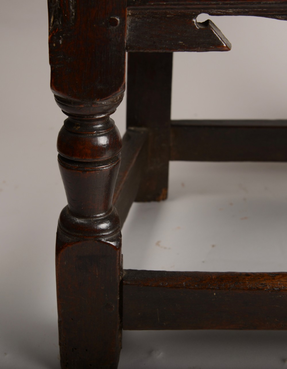 An early seventeenth-century dark oak wainscot armchair with a carved geometric panel back, turned arm supports, and a solid wooden seat. View VI