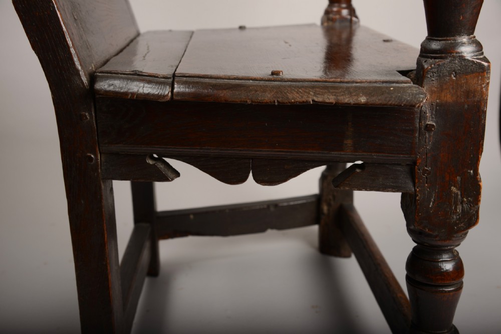 An early seventeenth-century dark oak wainscot armchair with a carved geometric panel back, turned arm supports, and a solid wooden seat. View VII