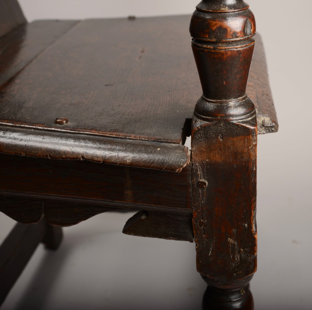 An early seventeenth-century dark oak wainscot armchair with a carved geometric panel back, turned arm supports, and a solid wooden seat. View VIII