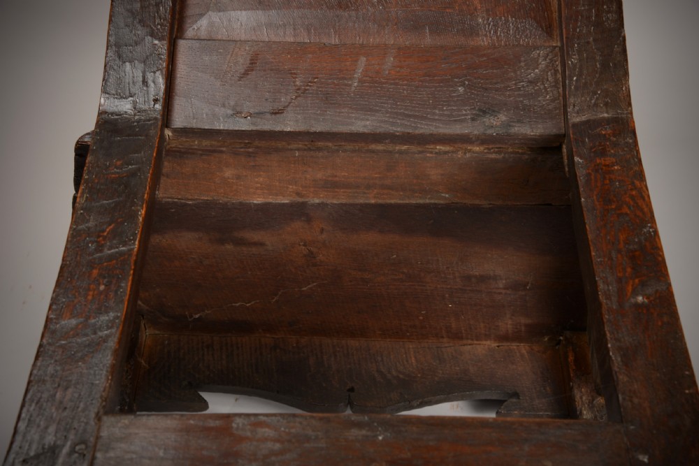 An early seventeenth-century dark oak wainscot armchair with a carved geometric panel back, turned arm supports, and a solid wooden seat. View IX