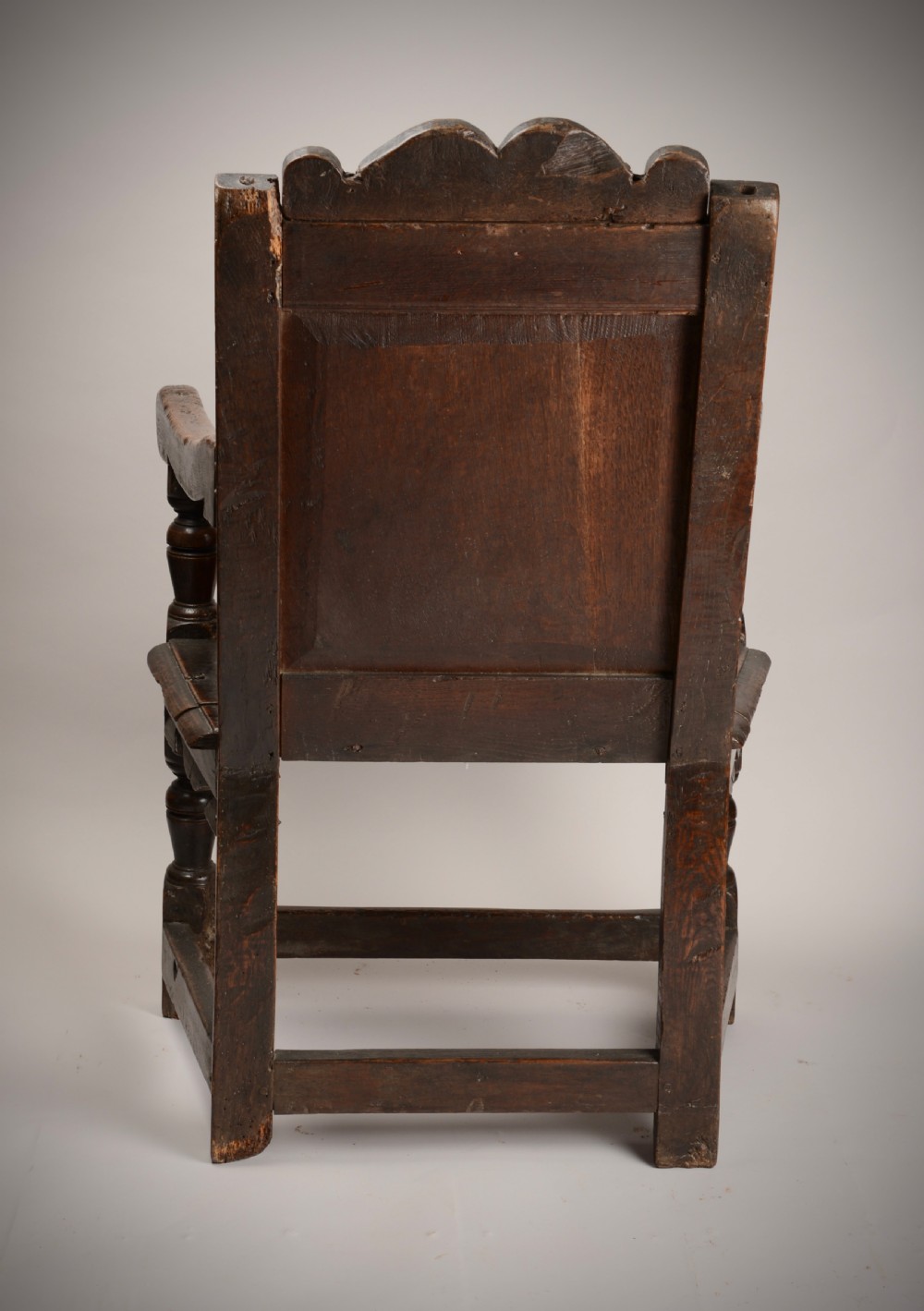 An early seventeenth-century dark oak wainscot armchair with a carved geometric panel back, turned arm supports, and a solid wooden seat. View X