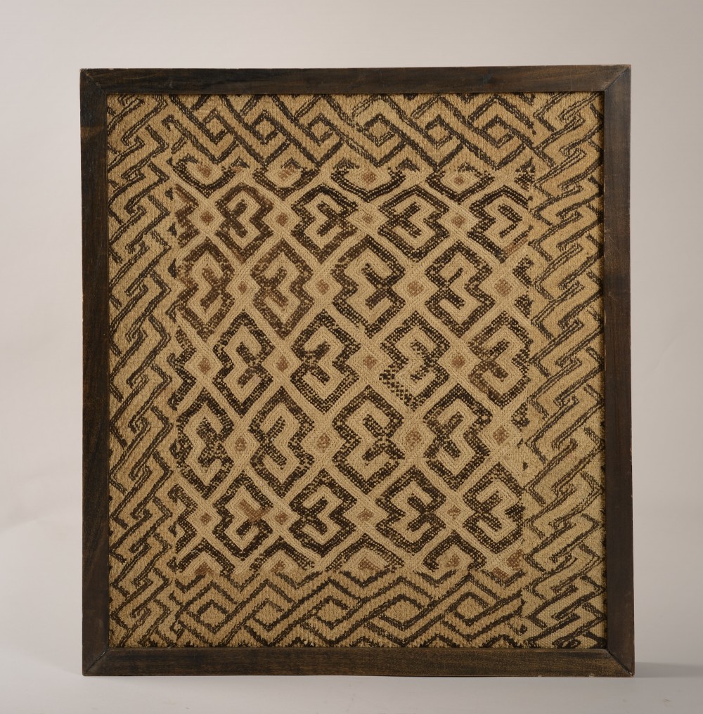 An early 20th-century framed Kuba cloth featuring geometric embroidered patterns woven from natural raffia fibres in shades of beige and dark brown.