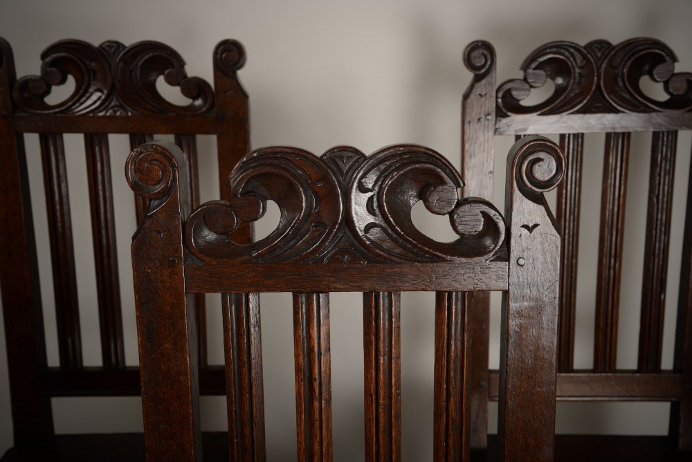 A set of four late seventeenth-century dark oak dining chairs featuring carved scroll top crestings, vertical back slats, solid panel seats, and turned stretchers. View II