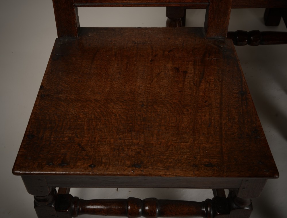 A set of four late seventeenth-century dark oak dining chairs featuring carved scroll top crestings, vertical back slats, solid panel seats, and turned stretchers. View III